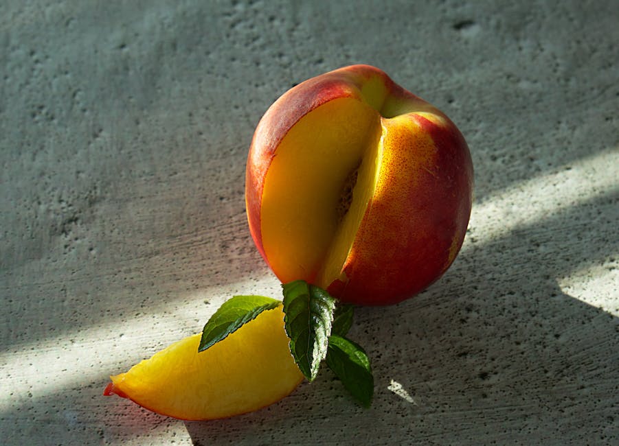 Close-up of a juicy peach with a slice and mint leaves in bright sunlight.